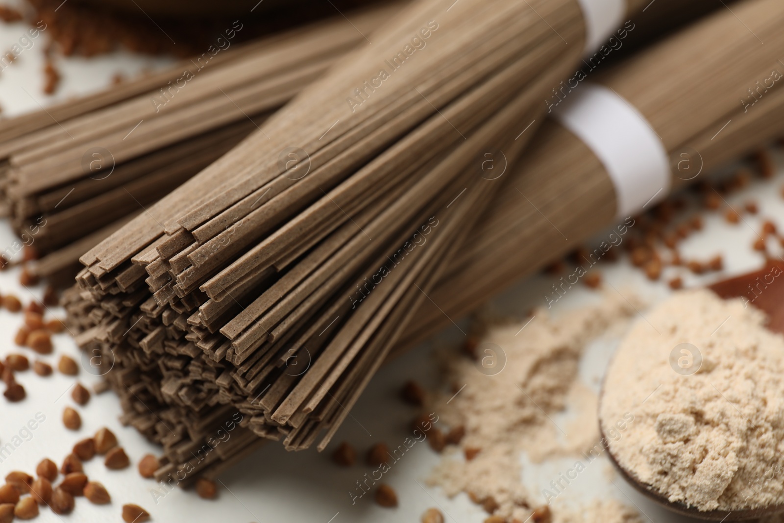Photo of Uncooked buckwheat noodles (soba), flour and grains on white table, closeup