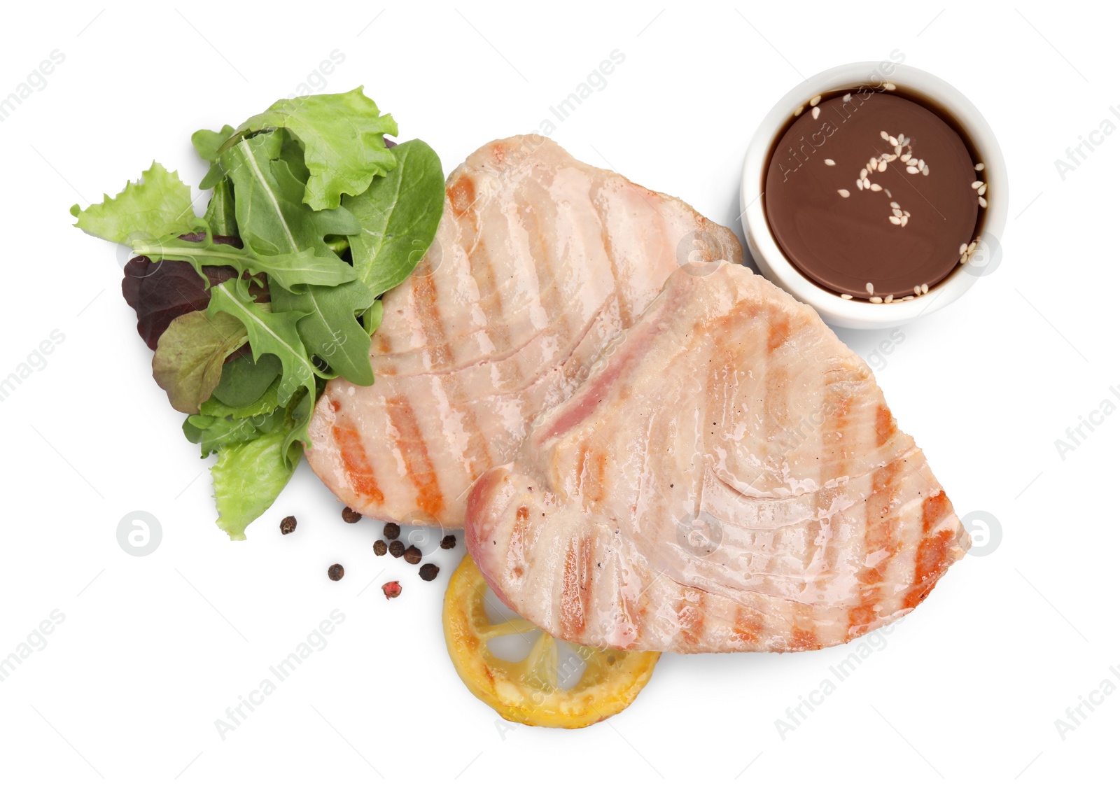 Photo of Delicious tuna steaks with salad, sauce and lemon isolated on white, top view