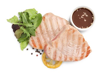 Photo of Delicious tuna steaks with salad, sauce and lemon isolated on white, top view