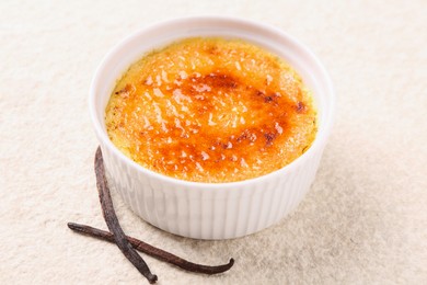 Delicious creme brulee in bowl and vanilla pods on light textured table, closeup