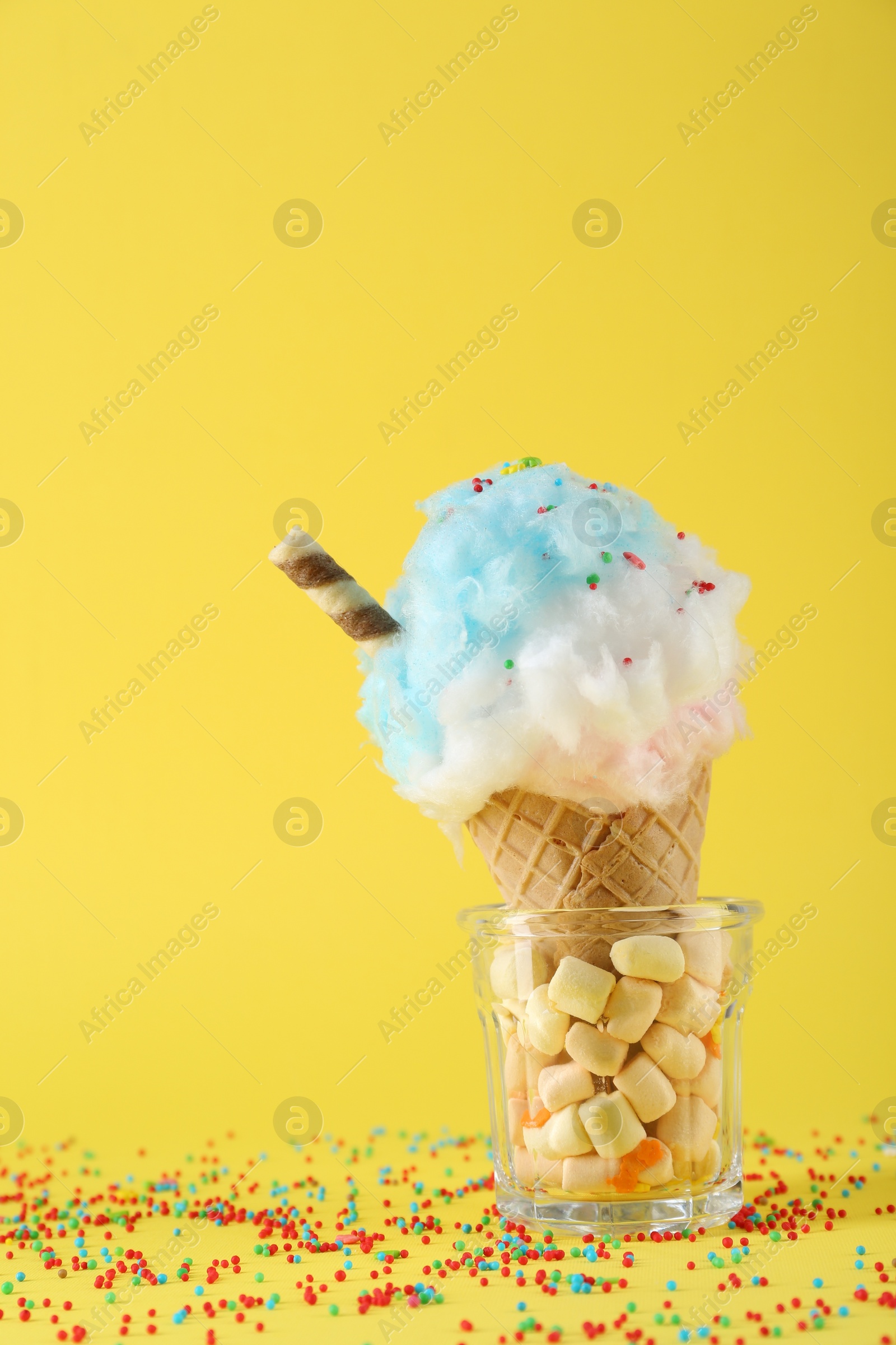 Photo of Sweet cotton candy in waffle cone on yellow background