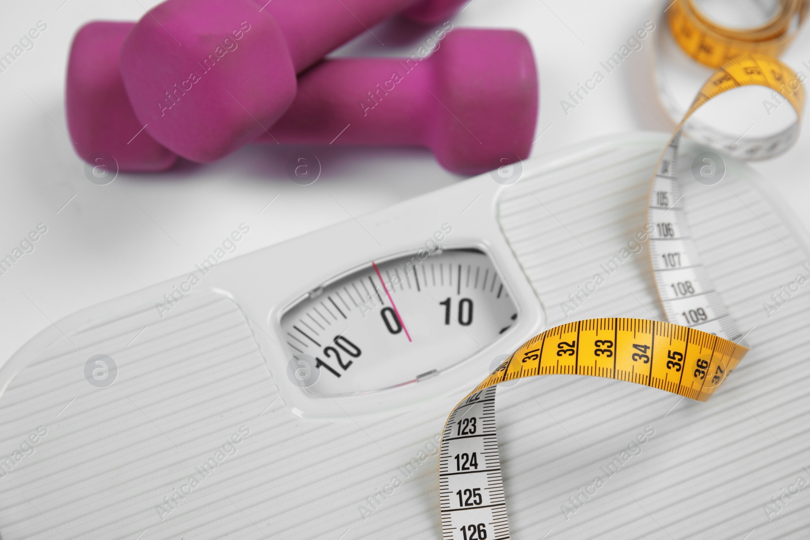 Photo of Modern scales, tape measure and dumbbells on white background, closeup