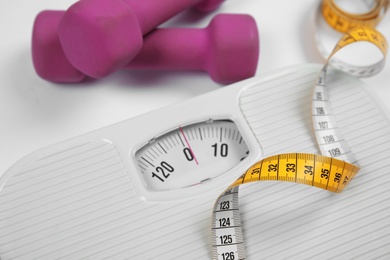 Modern scales, tape measure and dumbbells on white background, closeup