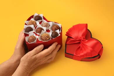 Photo of Woman with heart shaped box of delicious chocolate candies on yellow background, closeup
