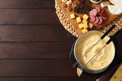 Fondue with tasty melted cheese, forks and different snacks on wooden table, top view. Space for text