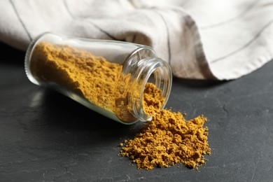 Photo of Jar with dry curry powder on dark textured table, closeup