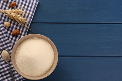 Photo of Uncooked organic semolina with spikelets and nuts on blue wooden table, flat lay. Space for text