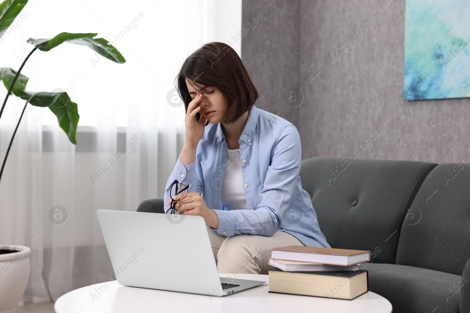 Photo of Overwhelmed woman with glasses sitting on sofa indoors
