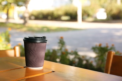 Photo of Cardboard coffee cup on wooden table outdoors. Space for text