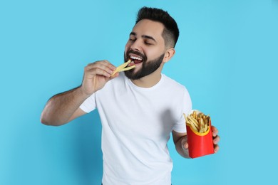 Young man eating French fries on light blue background