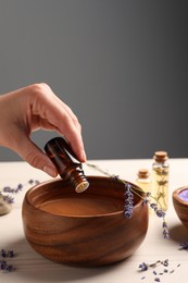 Woman dripping lavender essential oil from bottle into bowl at white wooden table, closeup. Space for text