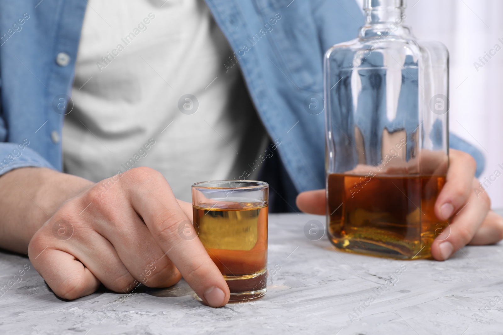 Photo of Alcohol addiction. Man with whiskey at grey textured table, closeup