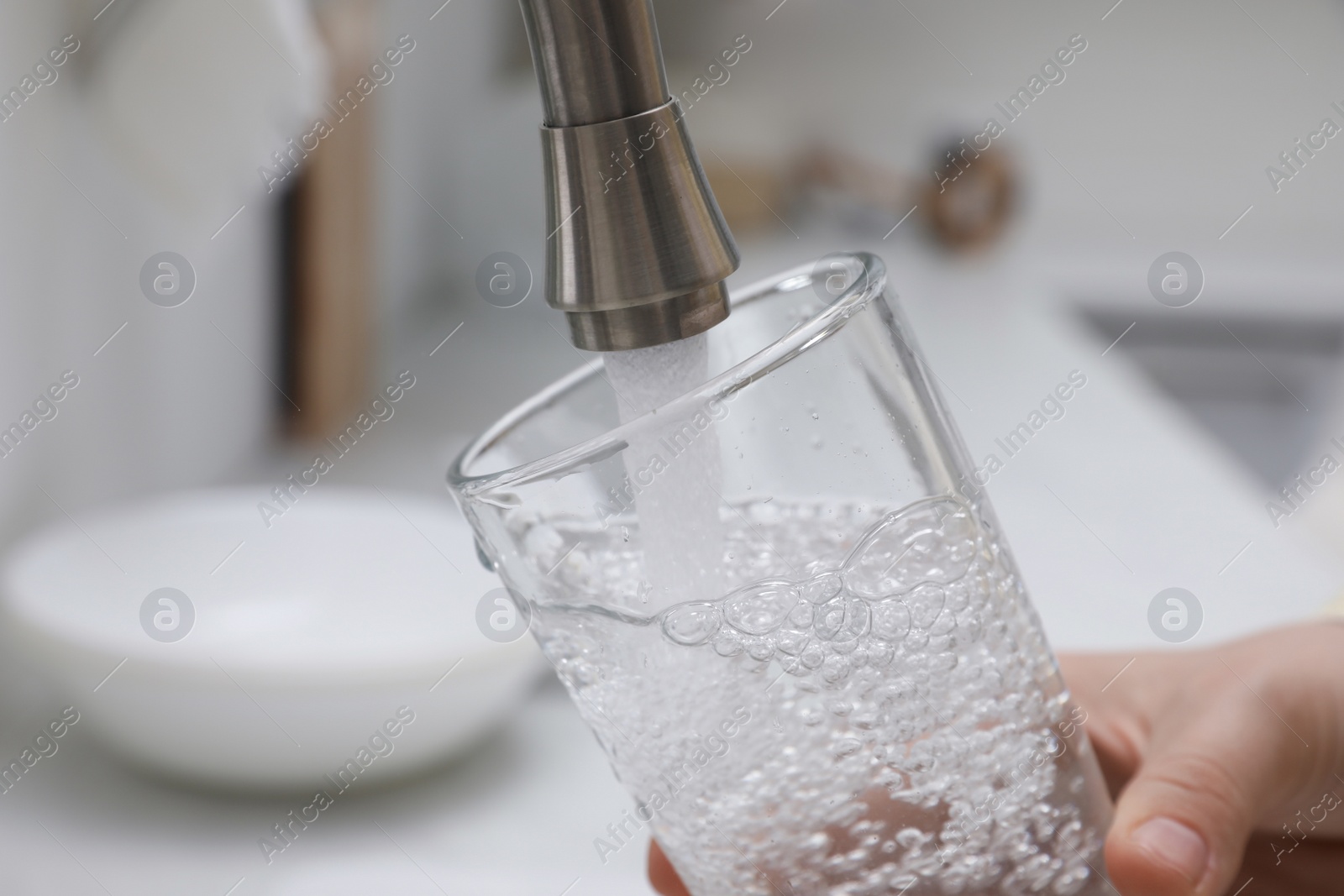 Photo of Woman filling glass with water from tap in kitchen, closeup