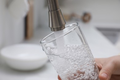 Woman filling glass with water from tap in kitchen, closeup