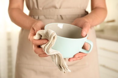 Woman wiping cup with towel in kitchen, closeup