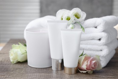 Photo of Cosmetic products, scented candle and folded towels with flowers on wooden table indoors