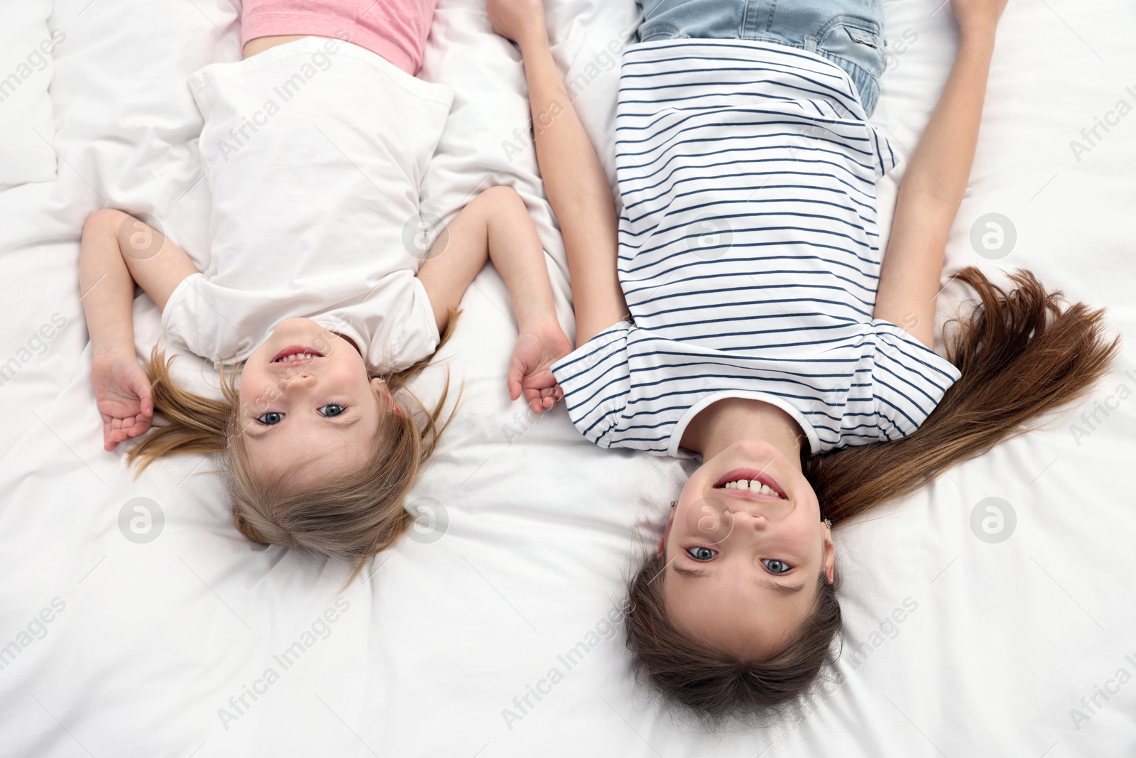 Photo of Cute little sisters on bed, top view