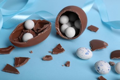 Tasty broken chocolate eggs with different sweets on light blue background
