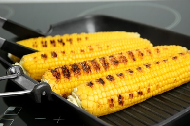 Photo of Cooking fresh corn cobs on grill pan, closeup