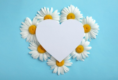 Flat lay composition with beautiful chamomile flowers and blank card on blue background, space for text