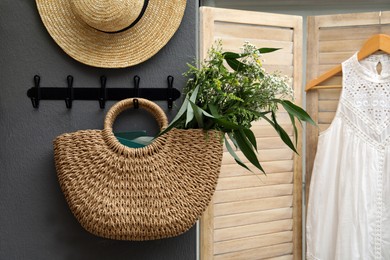 Photo of Stylish beach bag with beautiful wildflowers and books hanging on dark grey wall