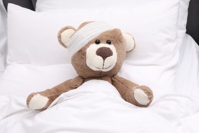Photo of Toy cute bear with bandage under blanket in bed