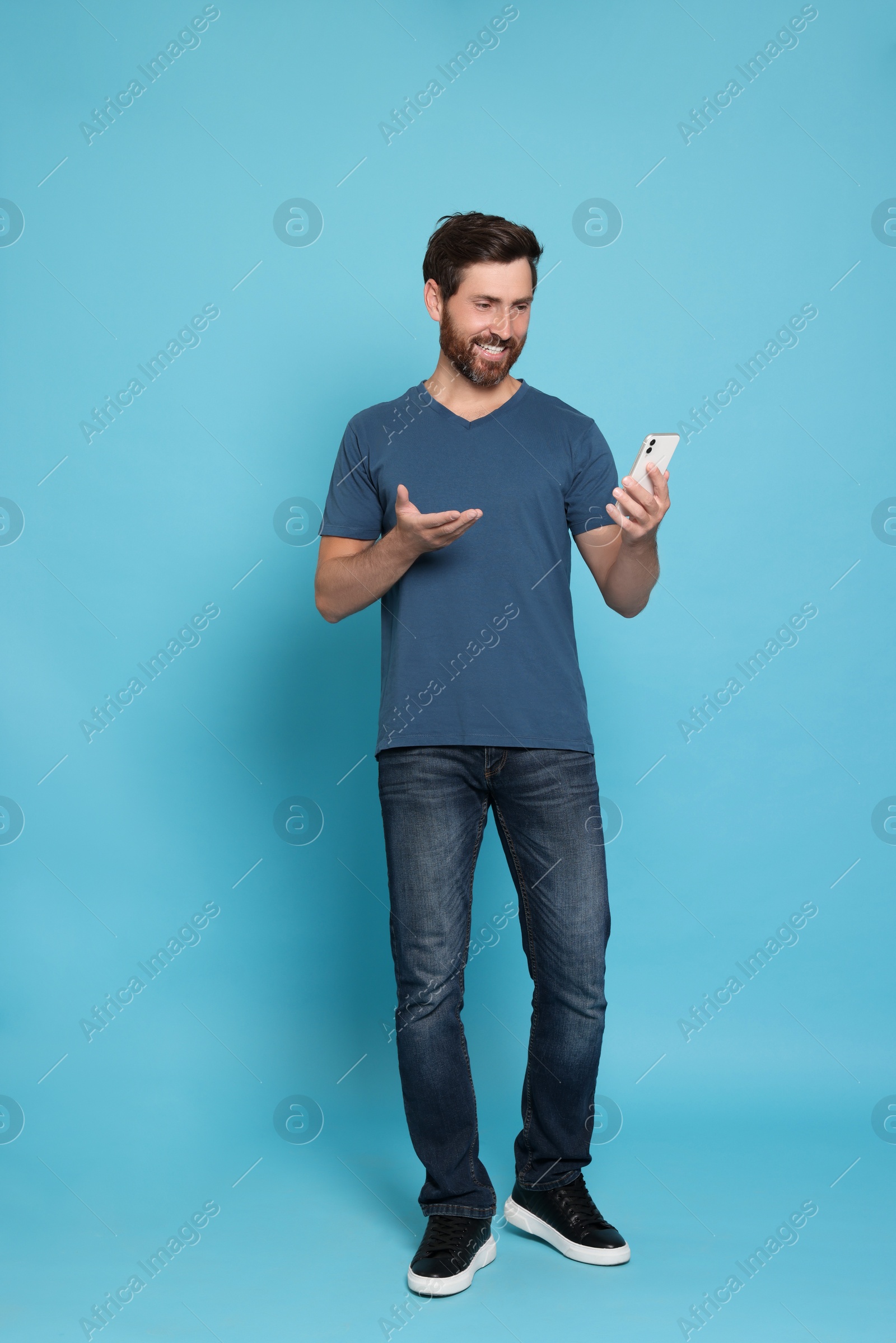 Photo of Handsome man having video chat on phone against light blue background