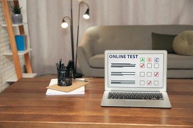 Photo of Laptop with online test and stationery on table at home