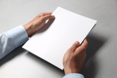Photo of Man holding blank notebook at light grey table, closeup. Mockup for design