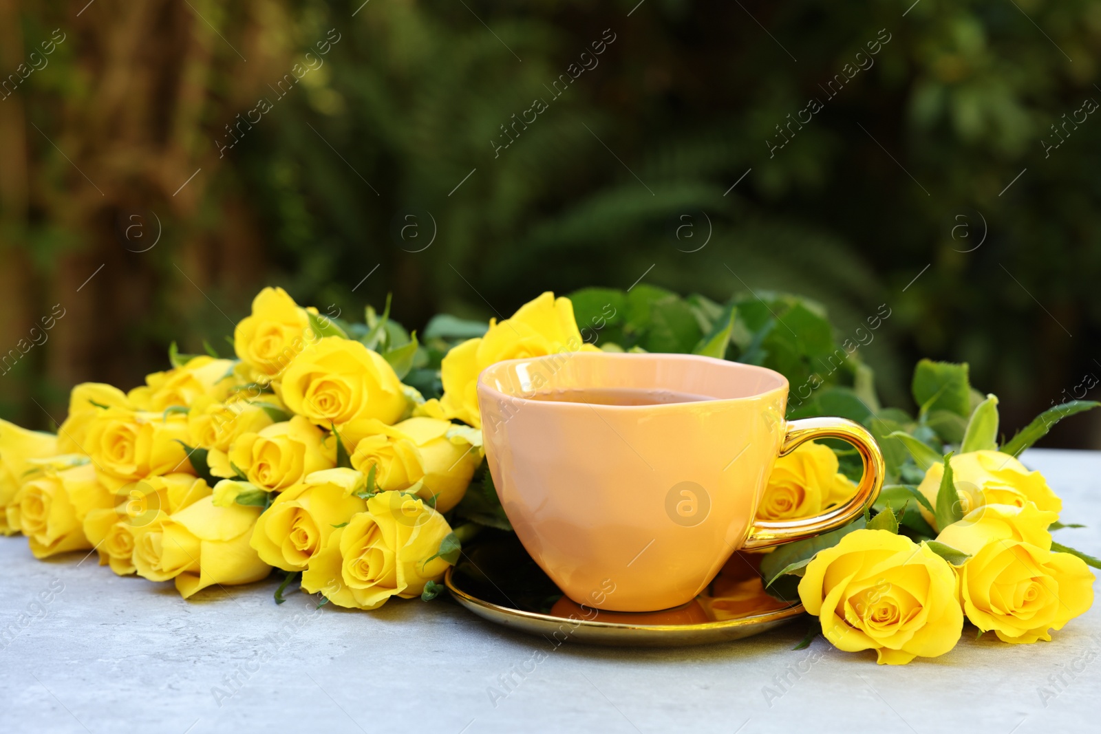 Photo of Cup of drink and beautiful yellow roses on light table outdoors