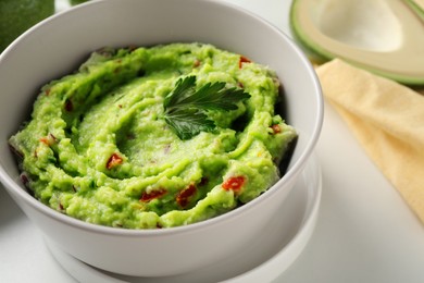 Photo of Bowl of delicious guacamole with parsley on white table, closeup