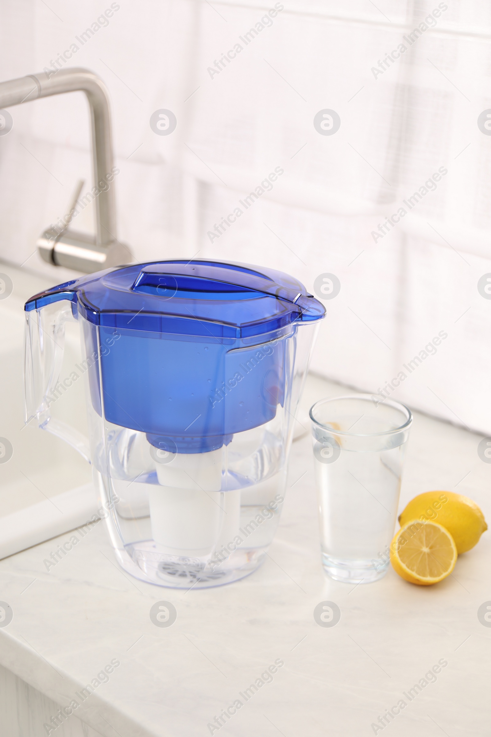 Photo of Water filter jug, glass and lemons on countertop in kitchen