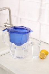 Photo of Water filter jug, glass and lemons on countertop in kitchen