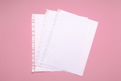 Punched pockets with paper sheets on pink background, flat lay. Space for text