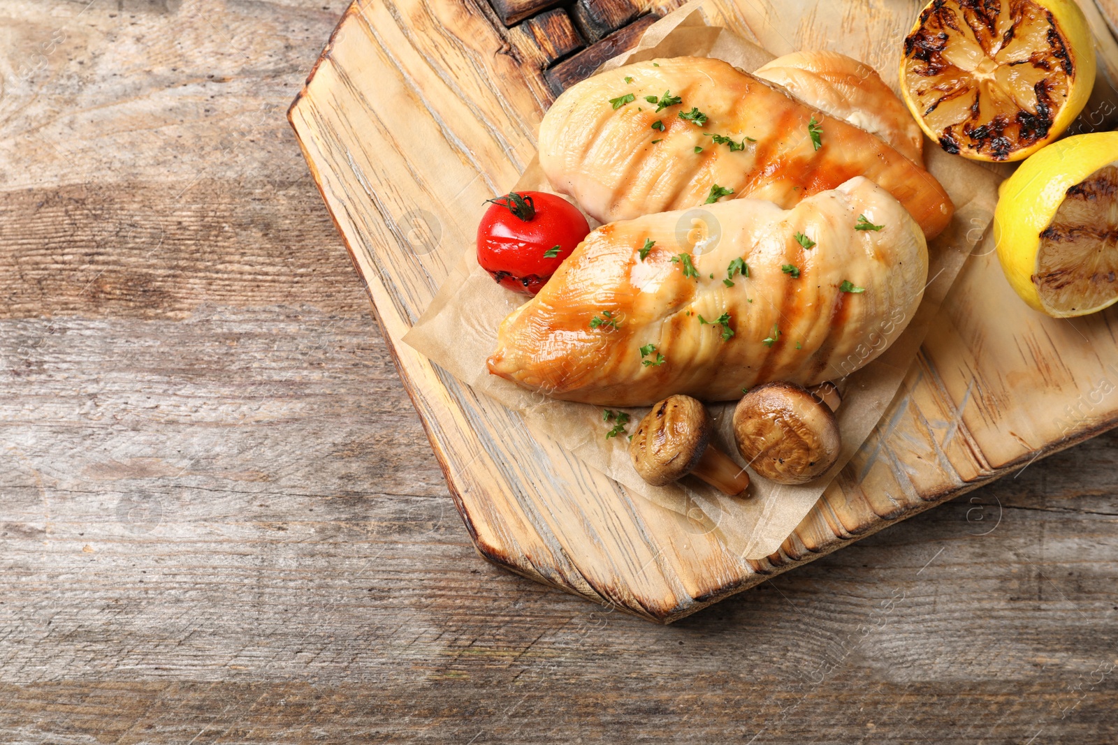 Photo of Board with grilled chicken breasts and garnish on wooden background, top view. Space for text