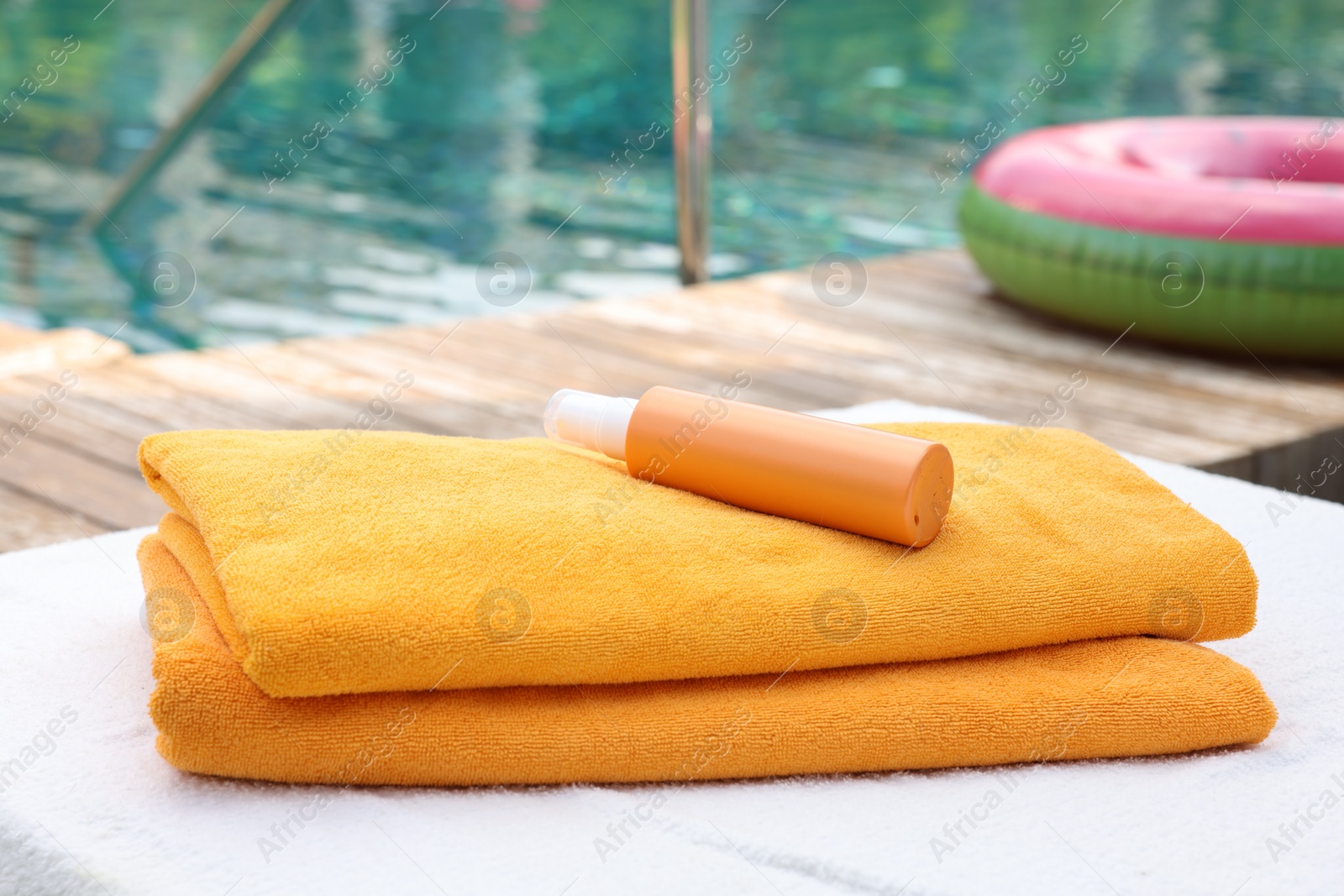 Photo of Beach towels and sunscreen on sun lounger near outdoor swimming pool, selective focus. Luxury resort