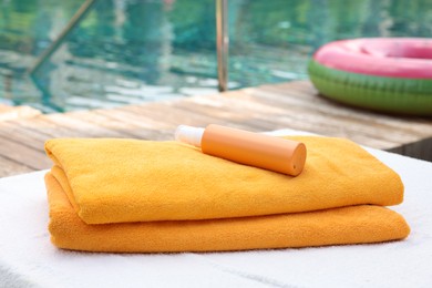 Photo of Beach towels and sunscreen on sun lounger near outdoor swimming pool, selective focus. Luxury resort