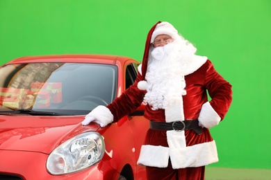 Authentic Santa Claus near car with presents against green background