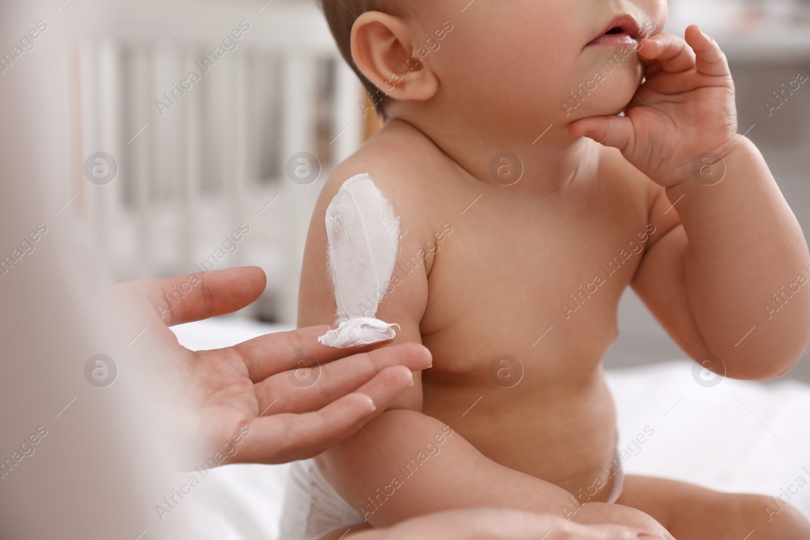 Photo of Mother applying moisturizing cream on her little baby at home, closeup