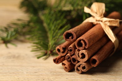 Photo of Bunch of cinnamon sticks and fir branches on wooden table, closeup. Space for text