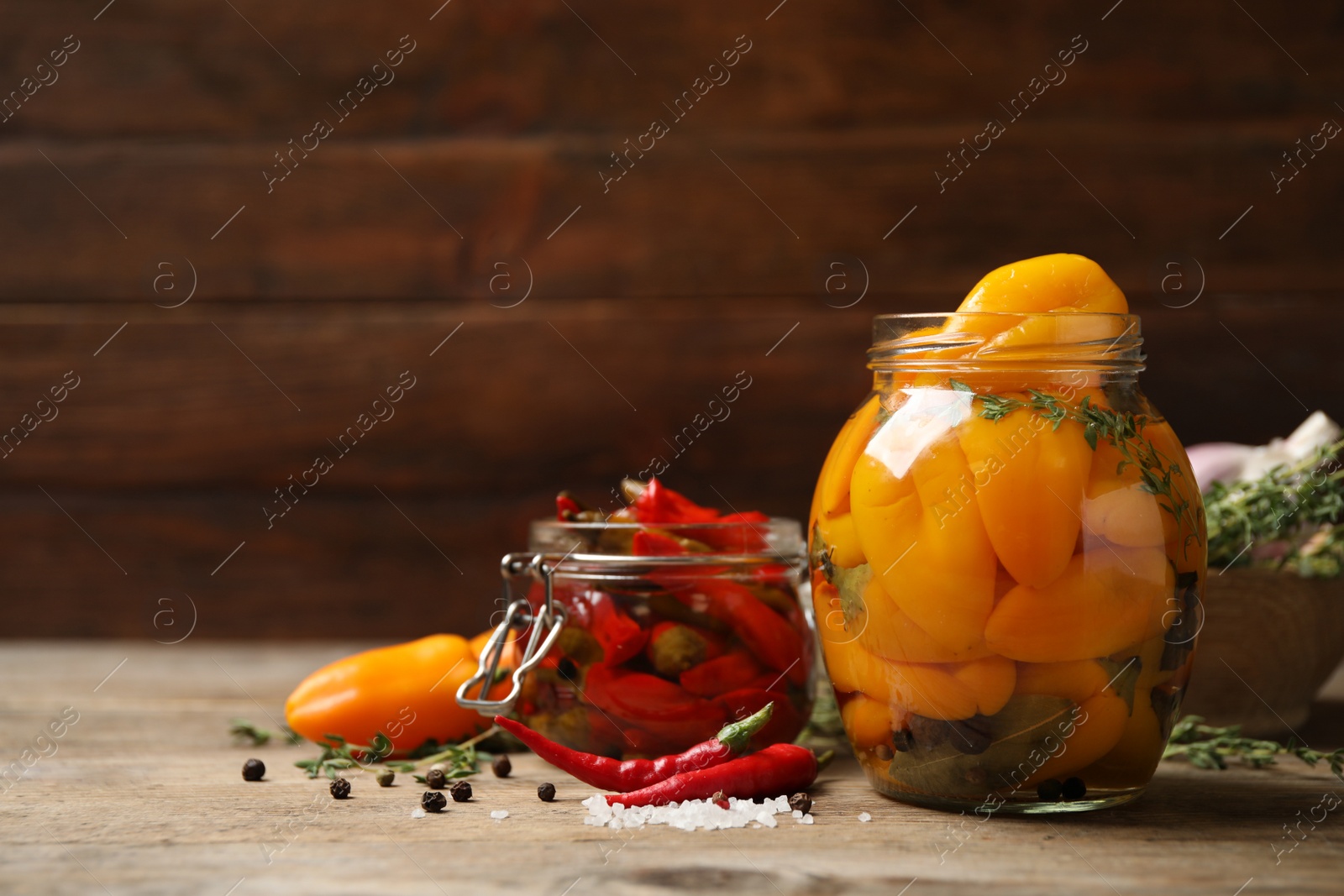 Photo of Glass jars with pickled peppers on wooden table. Space for text