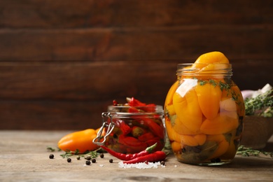 Glass jars with pickled peppers on wooden table. Space for text