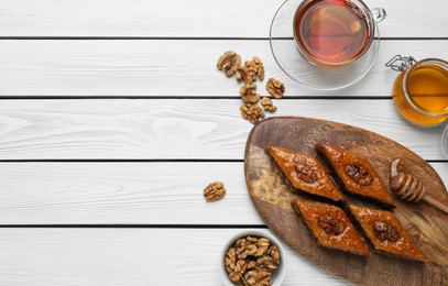 Photo of Delicious sweet baklava with walnuts, honey and hot tea on white wooden table, flat lay. Space for text