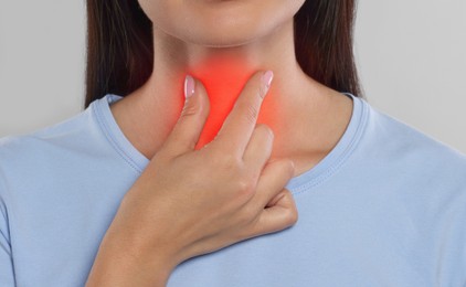 Endocrine system. Woman doing thyroid self examination on light grey background, closeup