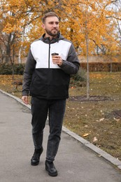 Photo of Handsome man wearing stylish clothes with cup of coffee in autumn park