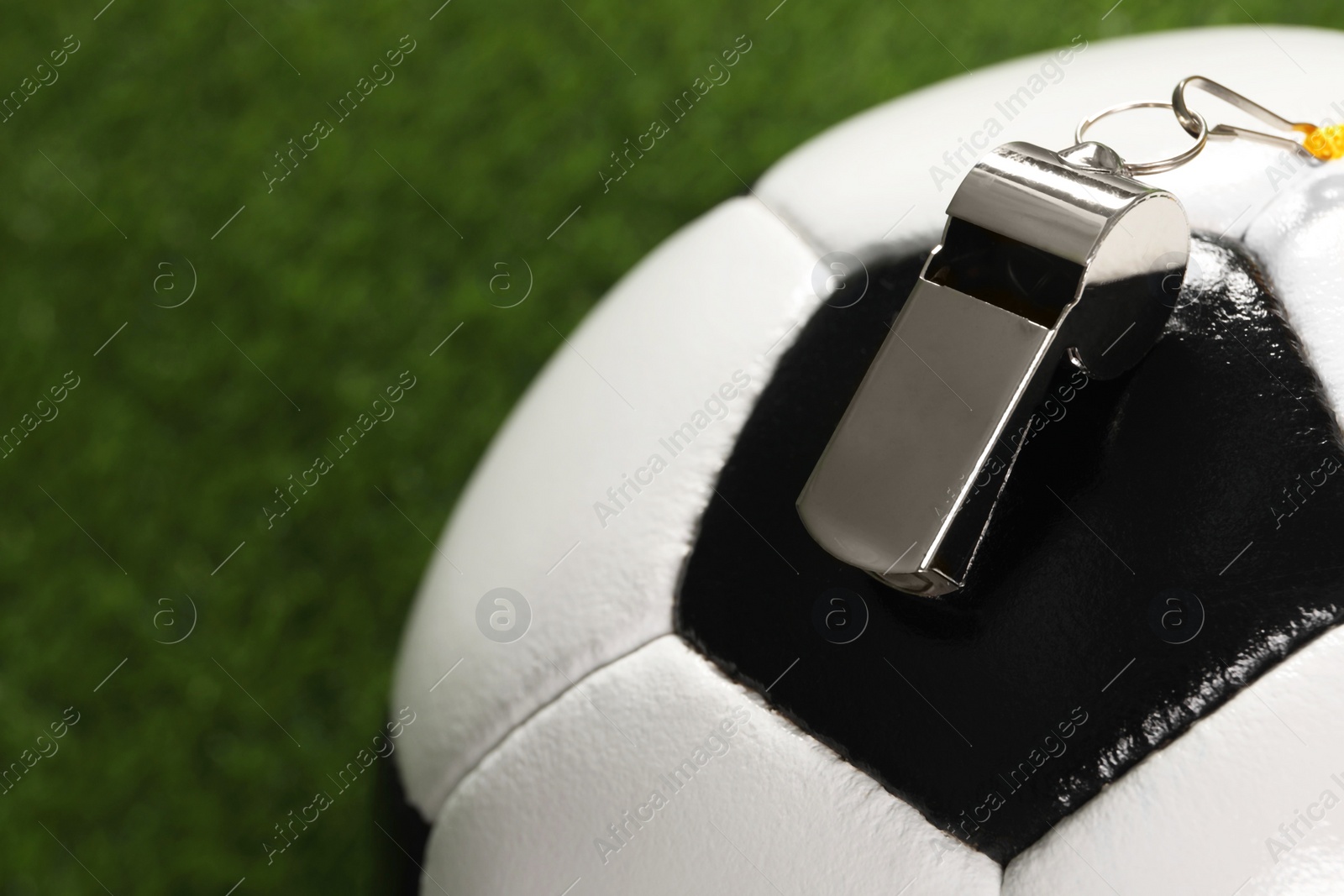 Photo of Football referee equipment. Soccer ball and metal whistle on green grass, closeup with space for text