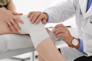 Photo of Orthopedist applying bandage onto patient's knee in clinic, closeup