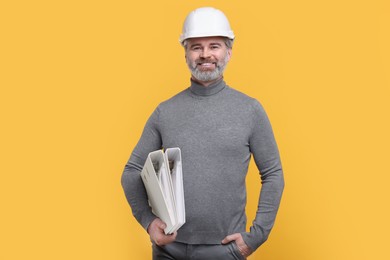 Photo of Architect in hard hat holding folders on orange background