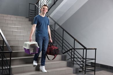 Travel with pet. Man holding carrier with cute cat and bag on stairs indoors