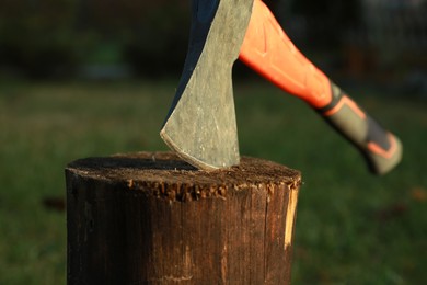 Photo of Metal axe in wooden log outdoors, closeup